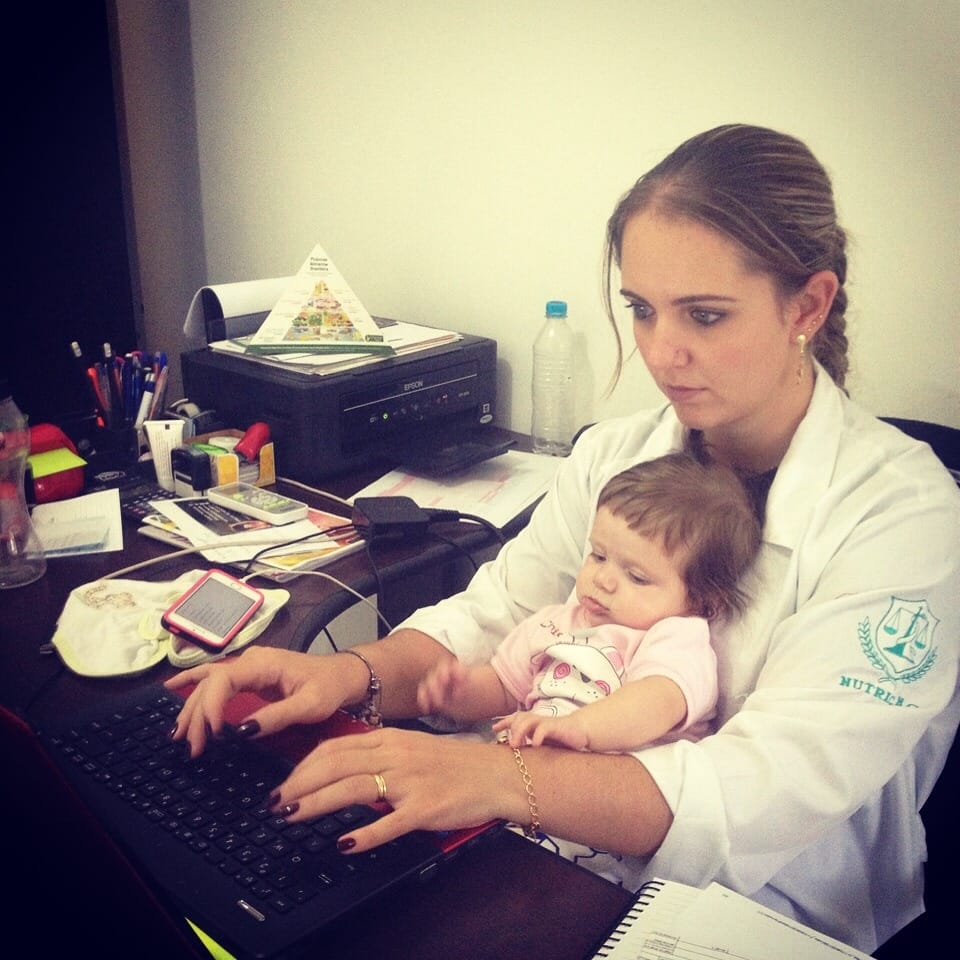 Carol Faria atendendo no consultório com a filha no colo